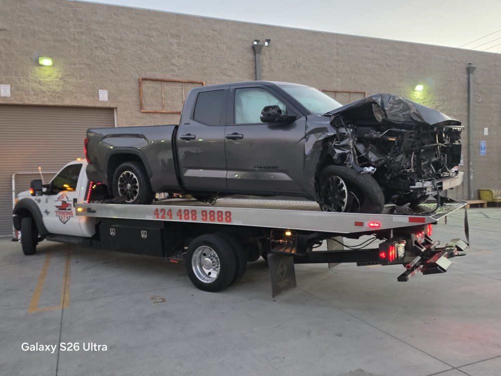 Towing GTA flatbed loaded with a collision-damaged pickup truck